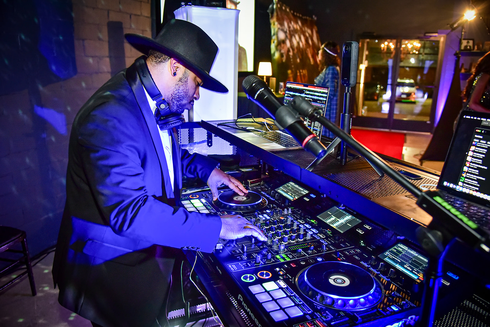 DJ One-Way mixing at the decks in a black hat and suit under blue lighting